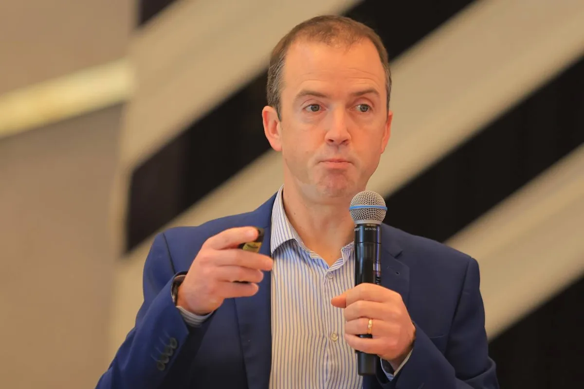 Paul Main speaking into a microphone at a conference